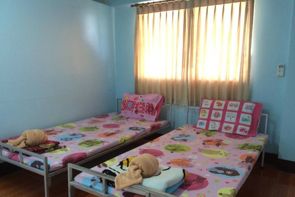 Dos camas individuales con ropa de cama colorida, una ventana con cortinas y suelo de madera.