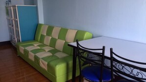 Una habitación con un sofá verde, una mesa blanca y dos sillas azules.
