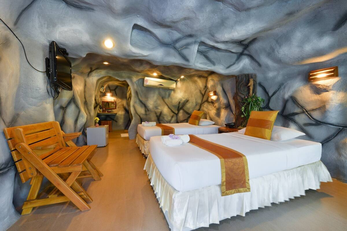 A room with a cave-like interior, featuring a bed, wooden chairs, a small table, and a television mounted on the wall.