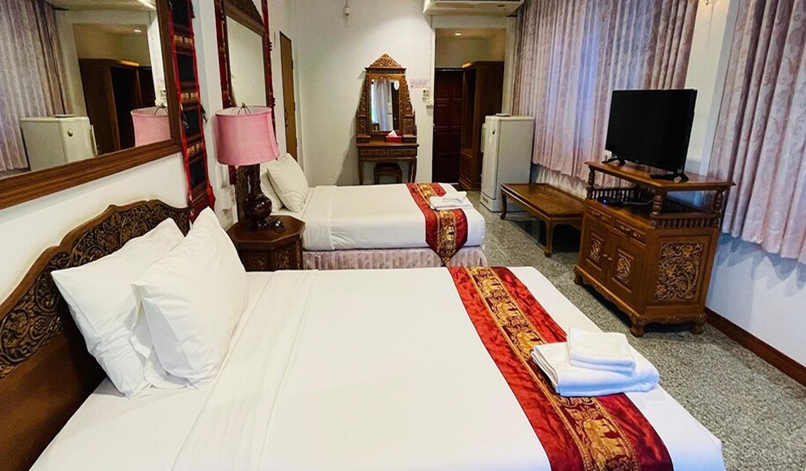 Une chambre d’hôtel avec deux lits, une télévision, un miroir et une commode en bois.