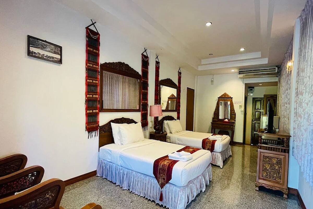 A hotel room with two beds, a wooden headboard, a mirror, a small table, and a cabinet.