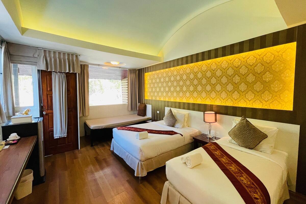 A hotel room with two beds, a desk, and a bench.