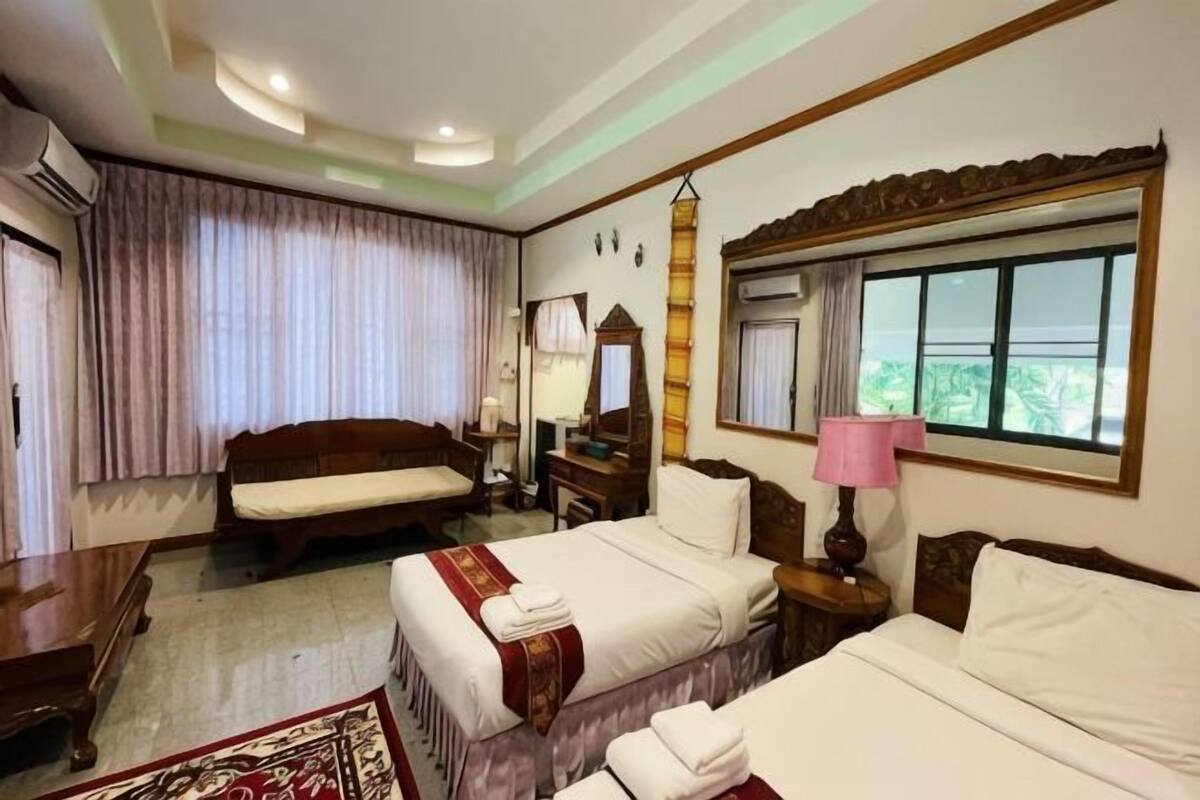A hotel room with two beds, a desk, a chair, a mirror, a window with curtains, and an air conditioning unit.
