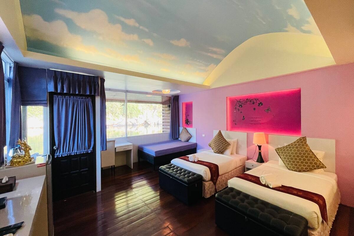 A hotel room with a bed, a desk, a window with curtains, a ceiling mural, and a nightstand with a lamp.