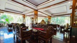 A spacious lobby with ornate wooden furniture, large windows with a view of greenery, and a high ceiling with decorative moldings. - Baan Rim Kwai Paerimnam Resort (Sai Yok)