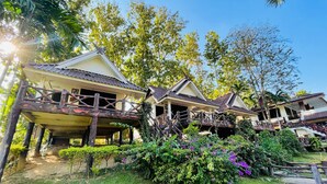 A traditional wooden house with a balcony, surrounded by lush greenery and a clear sky. - Baan Rim Kwai Paerimnam Resort (Sai Yok)