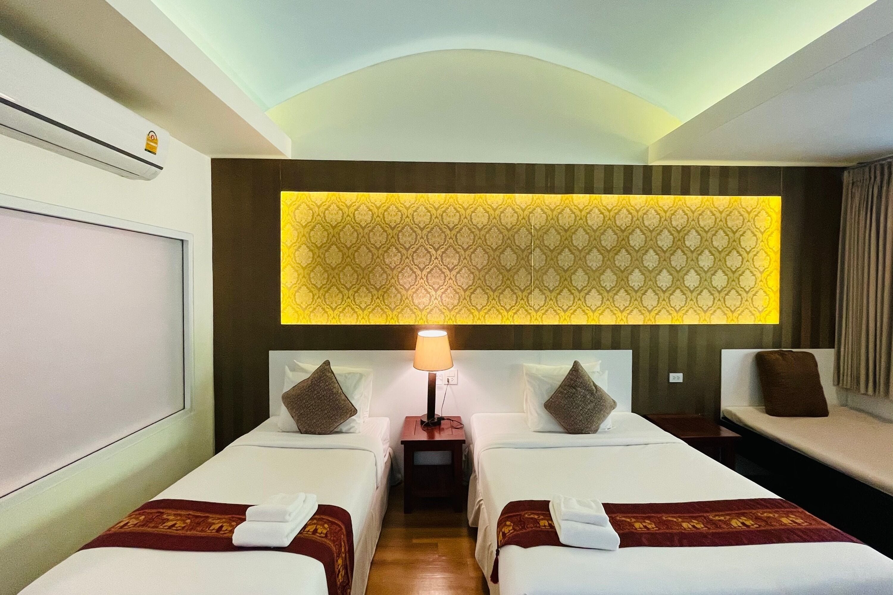 A hotel room with two beds, a nightstand with a lamp, and a patterned wall.