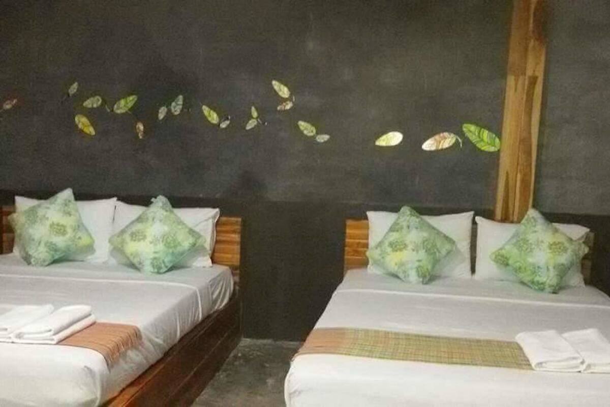 Zwei Einzelbetten mit weißen Bettwäsche und grün gemusterten Kissen in einem Zimmer mit dunkler Wand und einem Holzbalken.