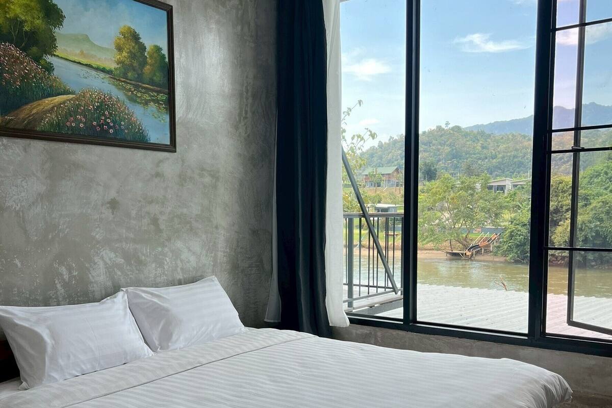Une chambre dotée d’une grande fenêtre donnant sur une rivière et un paysage verdoyant.