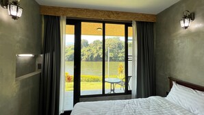 Quarto de hotel com uma cama grande, vista para um lago e varanda com mesa e cadeiras.