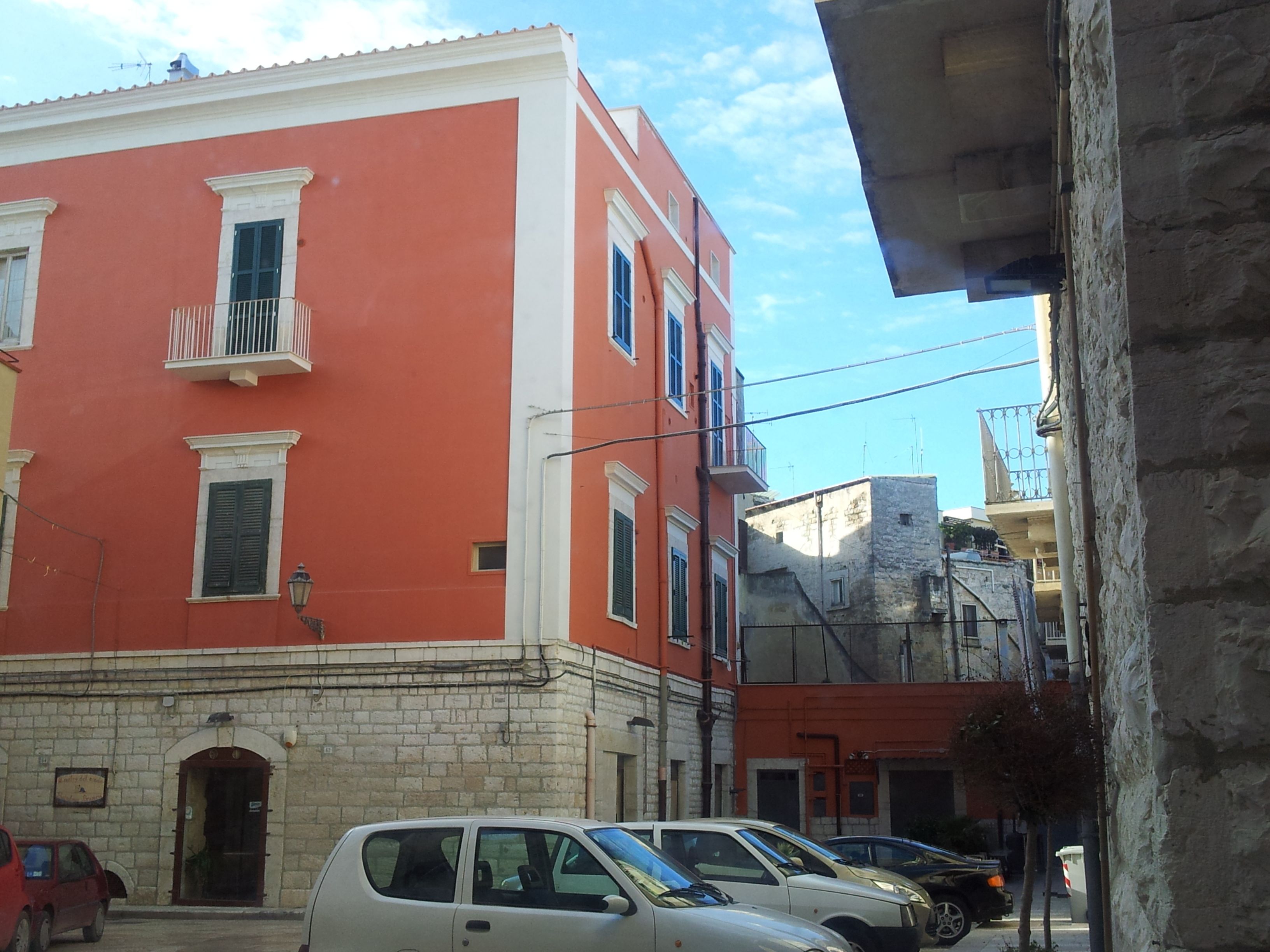 A street view with a red building, parked cars, and a stone wall.