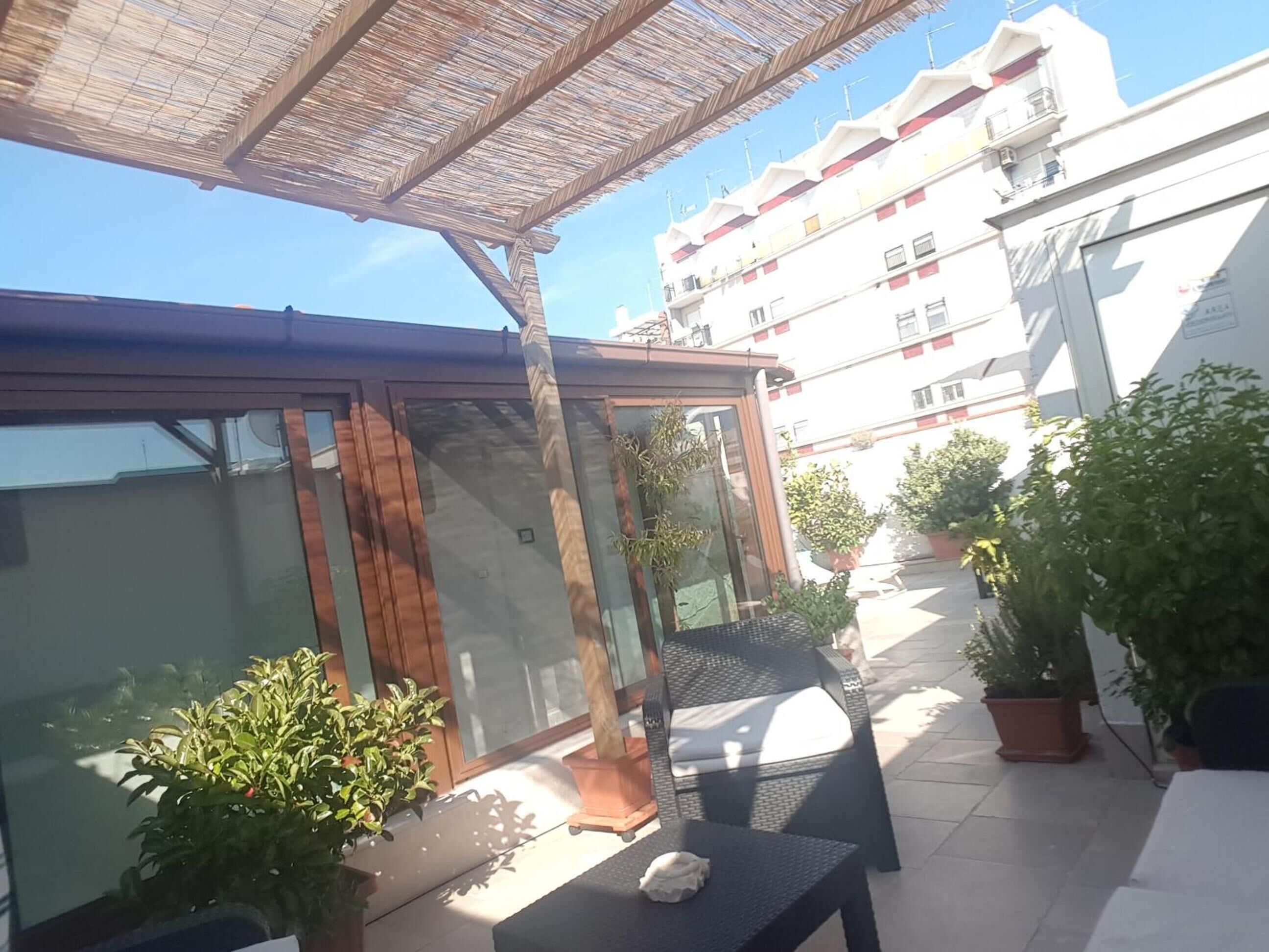 A covered patio area with a glass enclosure, outdoor furniture, and potted plants.
