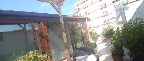 A covered patio area with a glass enclosure, outdoor furniture, and potted plants.