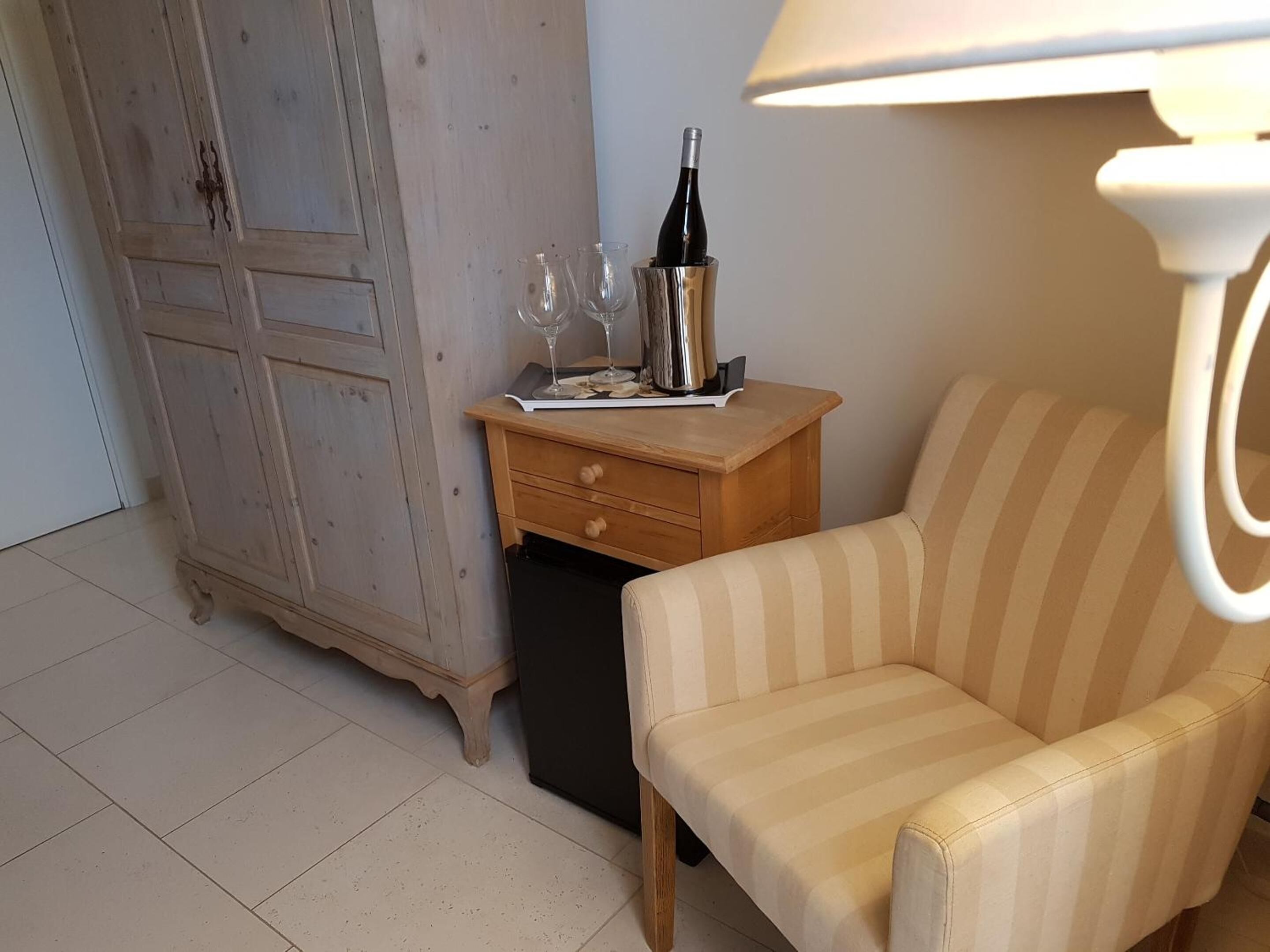 A room with a wooden cabinet, a small wooden nightstand with a lamp, a striped sofa, and a trash bin.