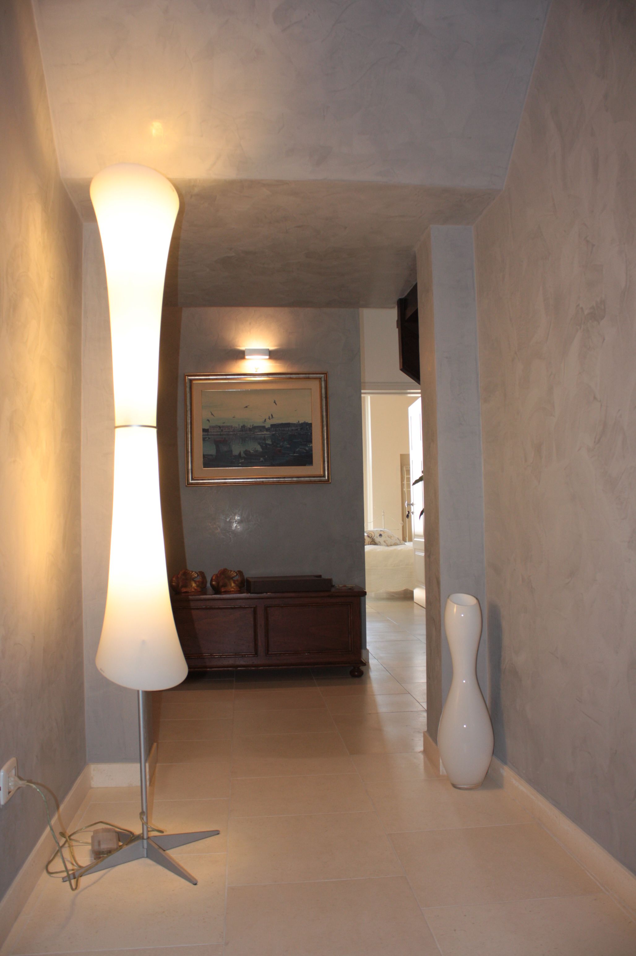 A hallway with a floor lamp, a painting on the wall, and a cabinet.