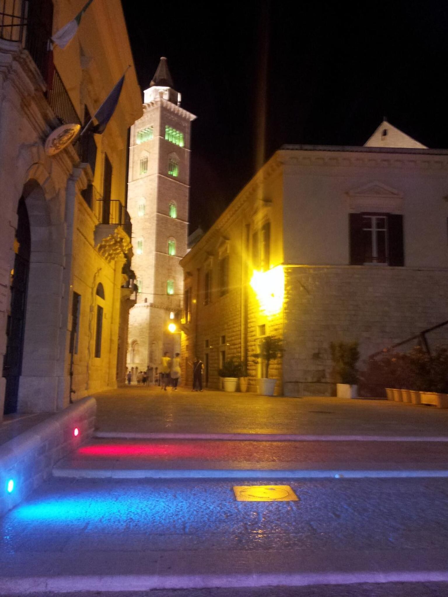 Vista nocturna de una plaza histórica con una torre destacada y un edificio con fachada iluminada.