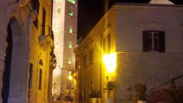 Vista nocturna de una plaza histórica con una torre destacada y un edificio con fachada iluminada.