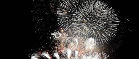 A nighttime fireworks display over a body of water with boats and a dock in the foreground.