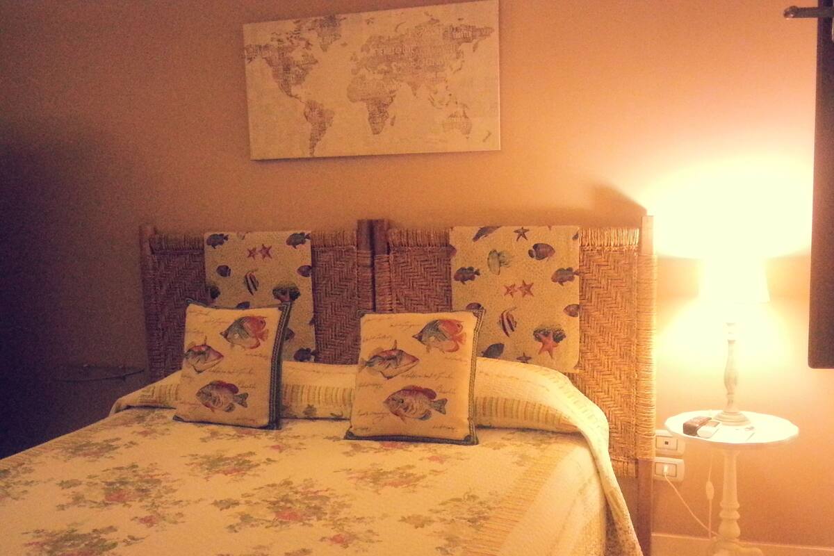 Una cama con ropa de cama floral, un mapa del mundo en la pared y una lámpara en una mesita de noche.