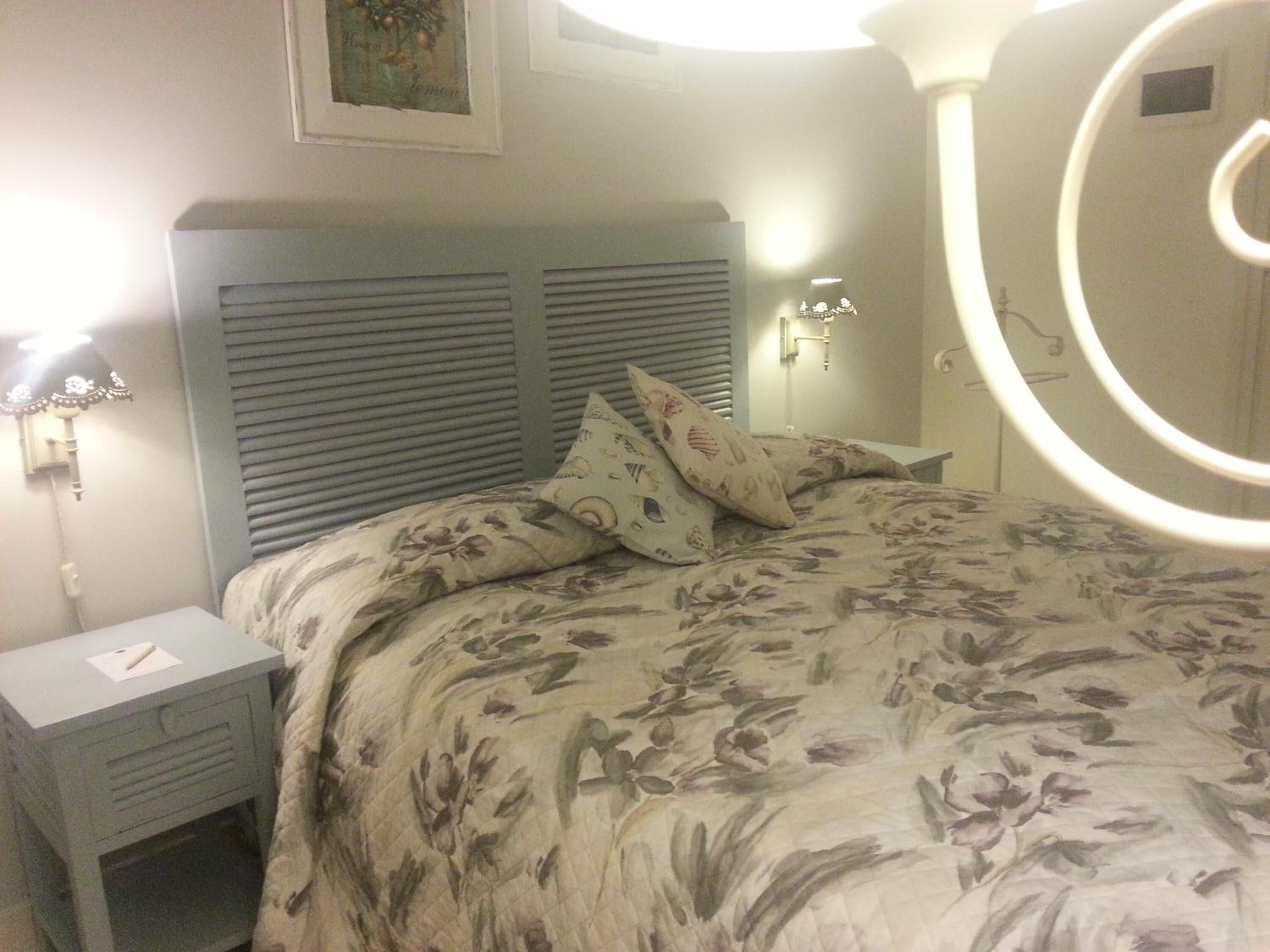 Un dormitorio con cama, mesita de noche, lámpara de pared y espejo.