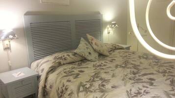Un dormitorio con cama, mesita de noche, lámpara de pared y espejo.