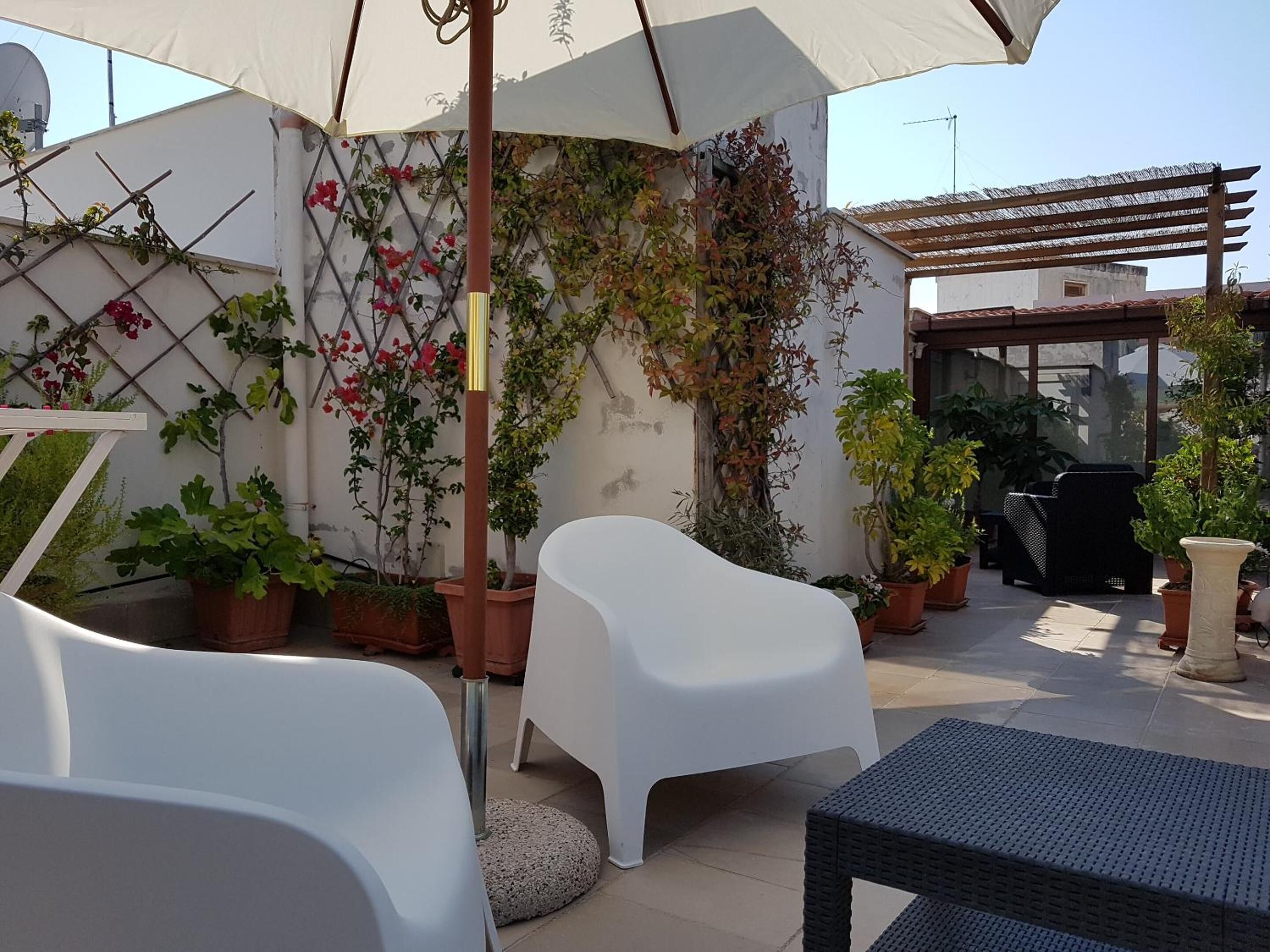 Un patio con sillas de plástico blanco, una mesa y varias plantas en macetas.