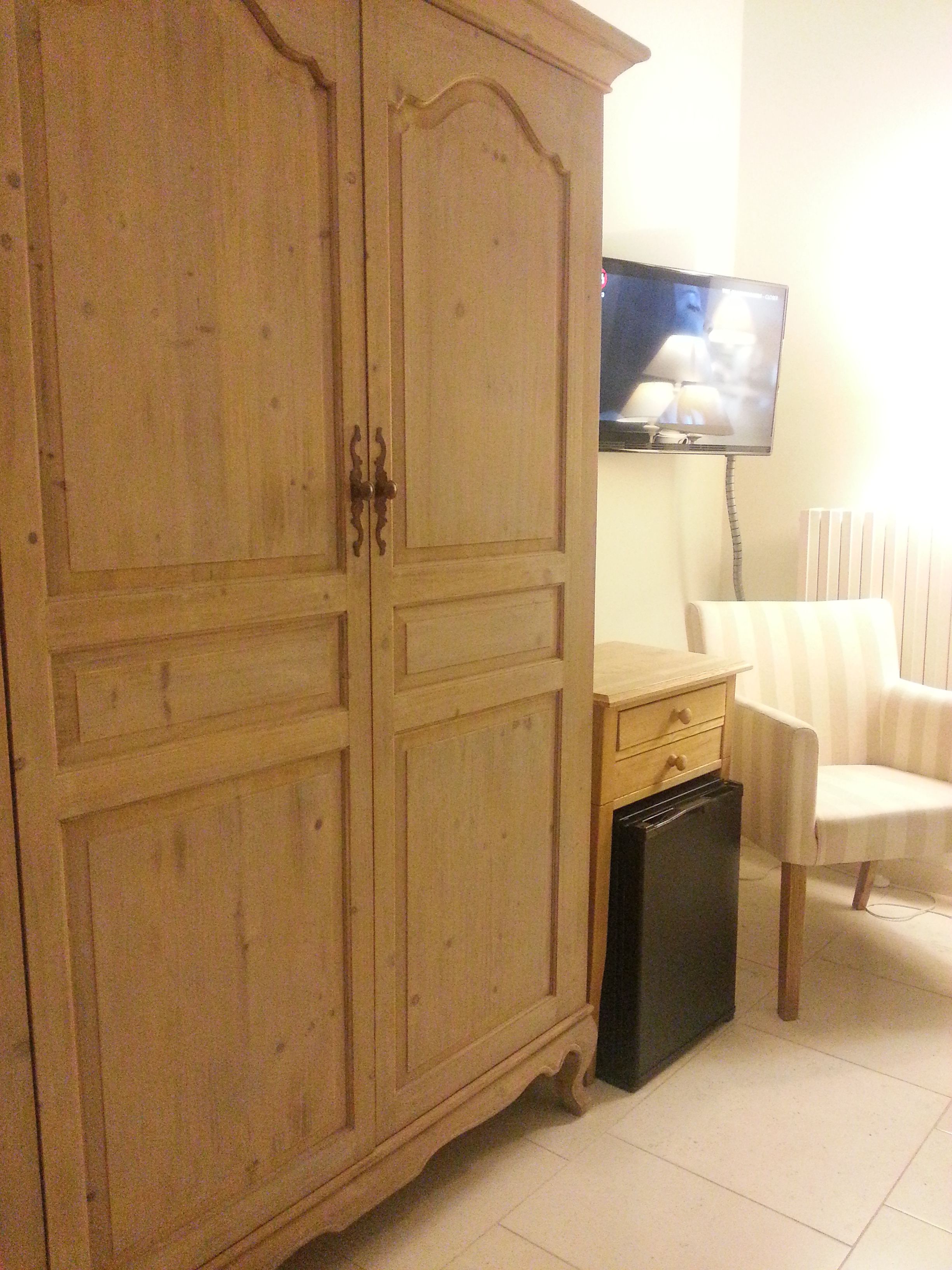 A room with a wooden wardrobe, a television, a chair, and a radiator.