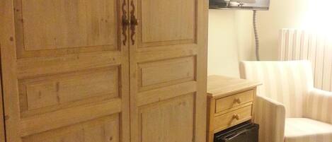 A room with a wooden wardrobe, a television, a chair, and a radiator.