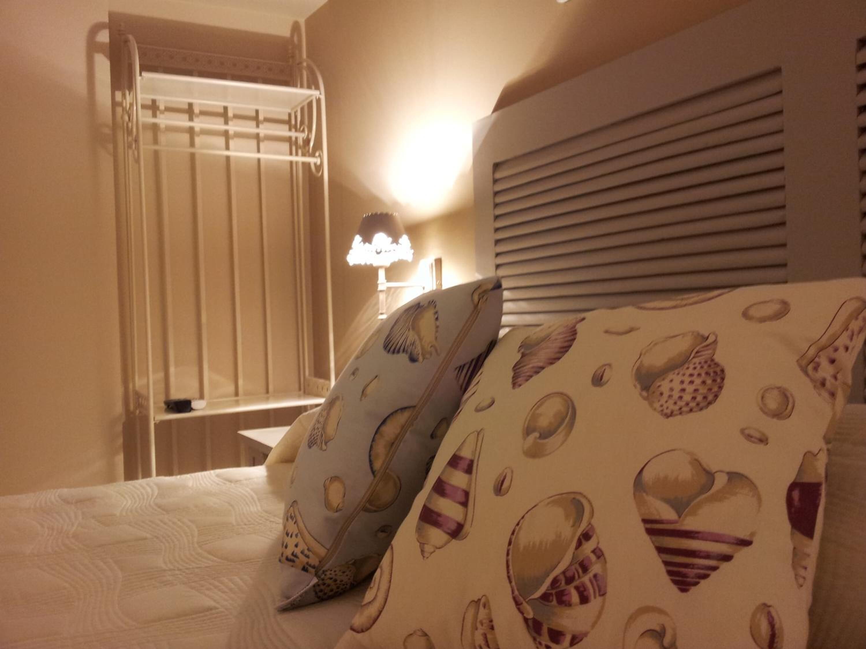 Een hotelkamer met een bed, nachtkastje, lamp en raam met zonwering.