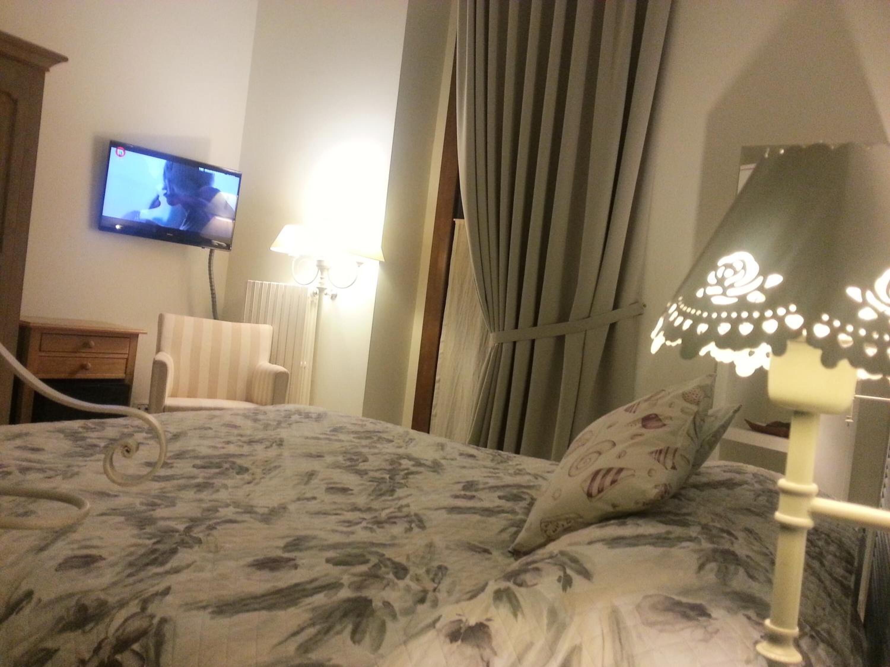 A hotel room with a bed, a television mounted on the wall, a lamp, and a window with curtains.