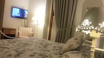 A hotel room with a bed, a television mounted on the wall, a lamp, and a window with curtains.