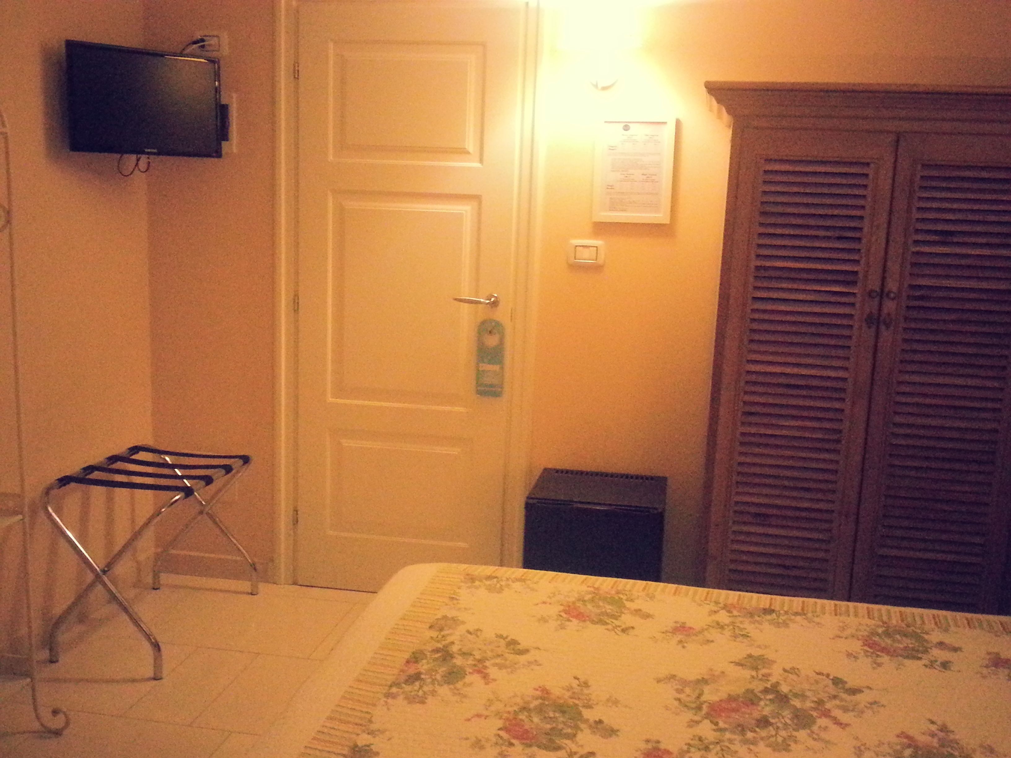Une chambre d’hôtel avec un lit, un téléviseur fixé au mur, une porte avec une serrure et une petite poubelle.