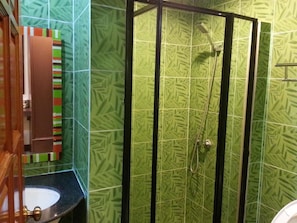 A bathroom with a green patterned tile wall, a black shower enclosure, and a sink with a wooden cabinet.