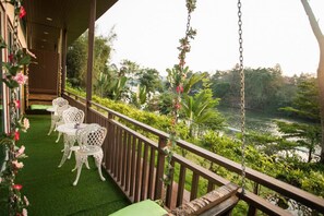 A balcony with white wicker chairs and a swing, overlooking a river and lush greenery. - Banana Resort & Spa (Kanchanaburi)