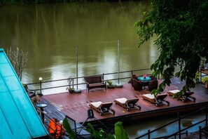 A wooden deck with lounge chairs and a table, overlooking a calm body of water.