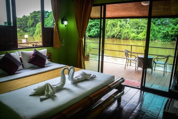 A hotel room with a bed, a balcony with a view of a river, and a table with chairs.