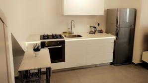Een kleine keuken met een gasfornuis, spoelbak en een roestvrijstalen koelkast.