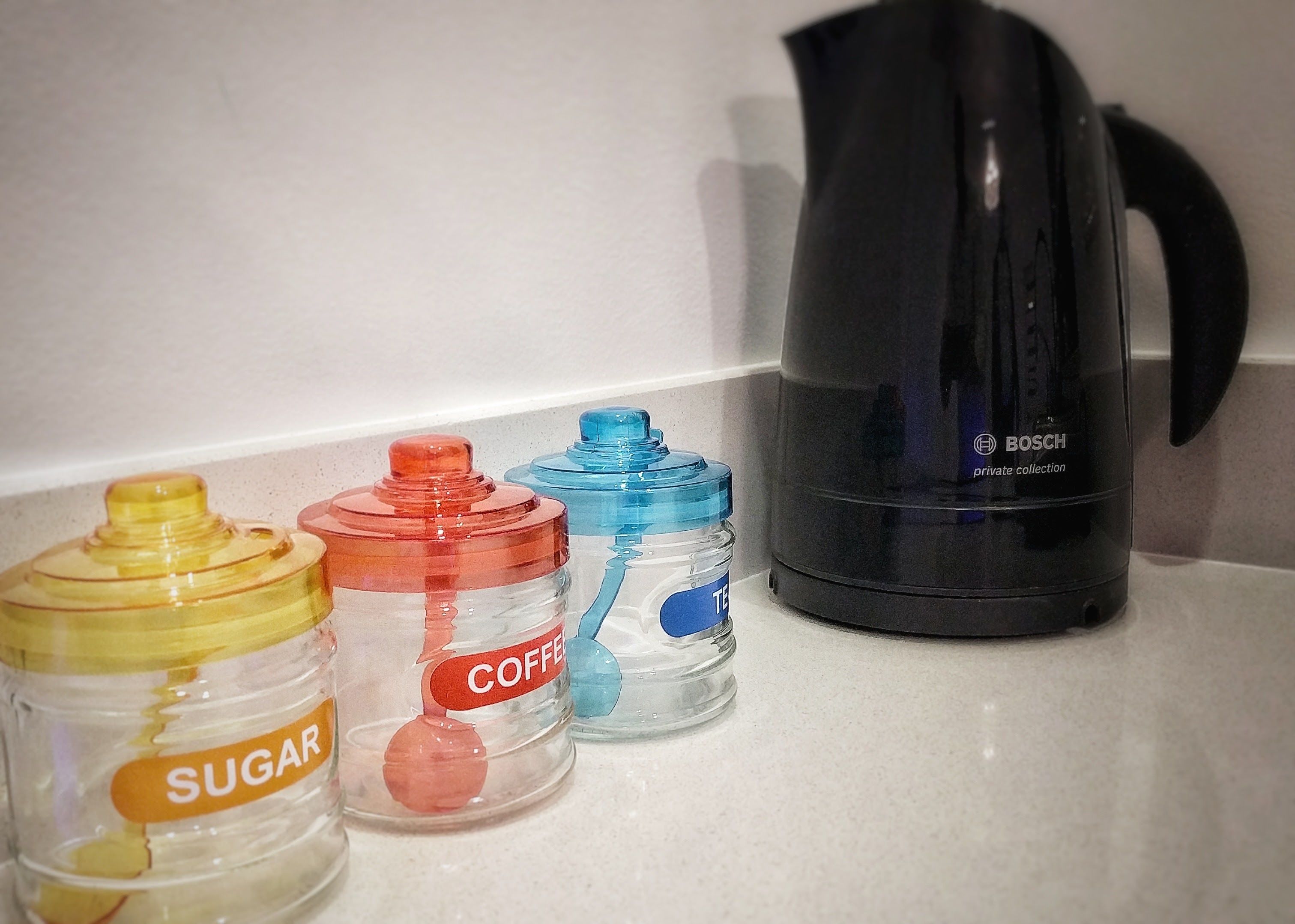 A kitchen counter with three containers labeled 'SUGAR', 'COFFEE', and 'TEA', and a black Bosch coffee maker.