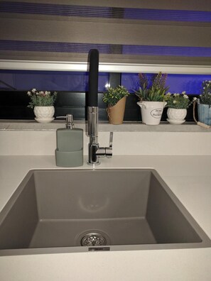 Un évier de cuisine moderne, doté d’un seul robinet, d’un petit meuble et d’une fenêtre agrémentée de plantes décoratives.
