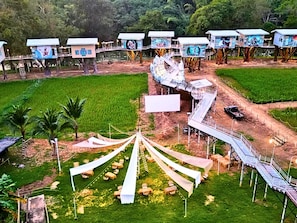 A series of elevated treehouse-style accommodations with a central walkway and surrounding fields. - Yoko River Kwai Resort (Sai Yok)