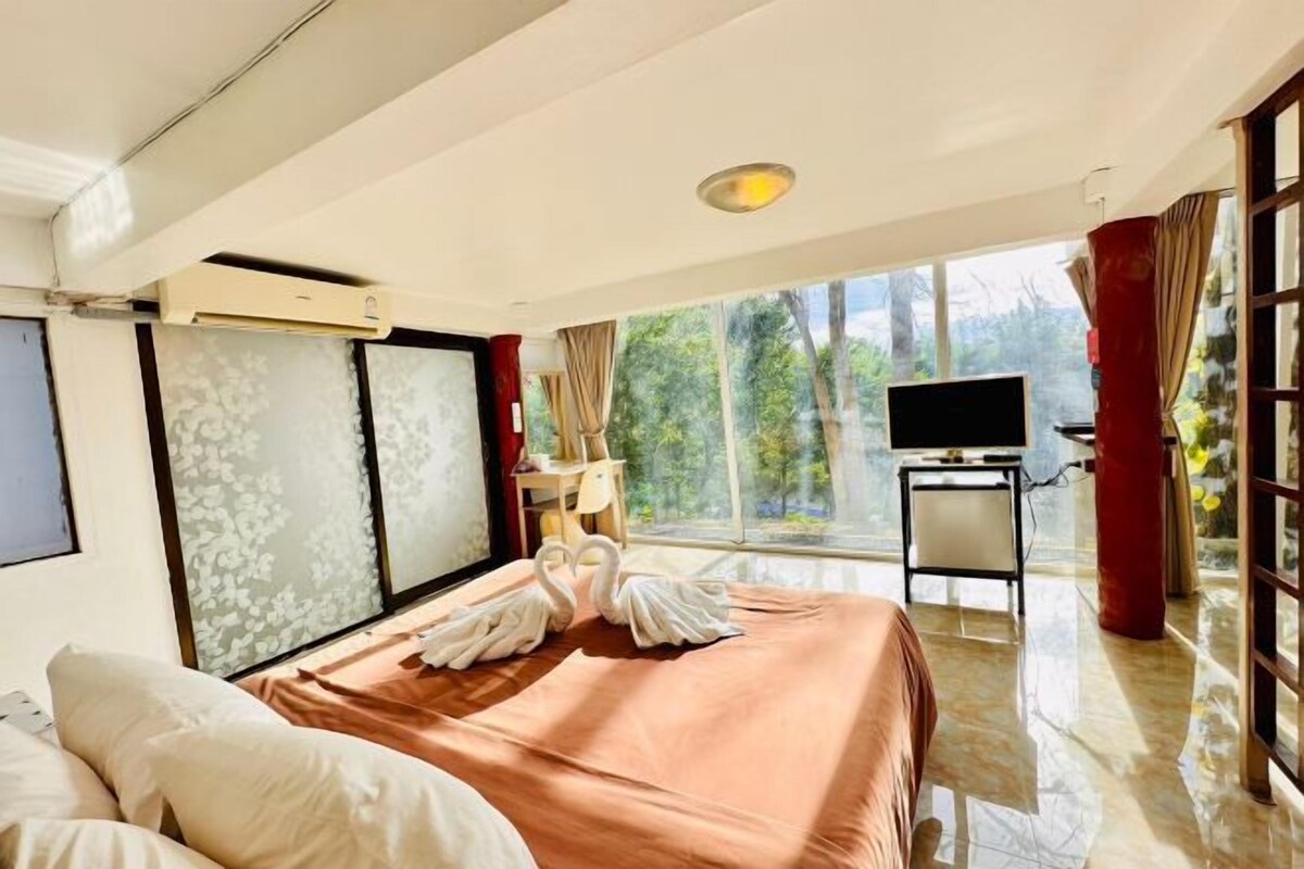 Une chambre d’hôtel avec un lit, une télévision, un bureau et une vue sur les arbres, visible à travers de grandes fenêtres.