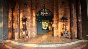 Una entrada de ladrillo con una puerta central que presenta una estatua de Buda, flanqueada por pilares de madera y decoración tradicional.