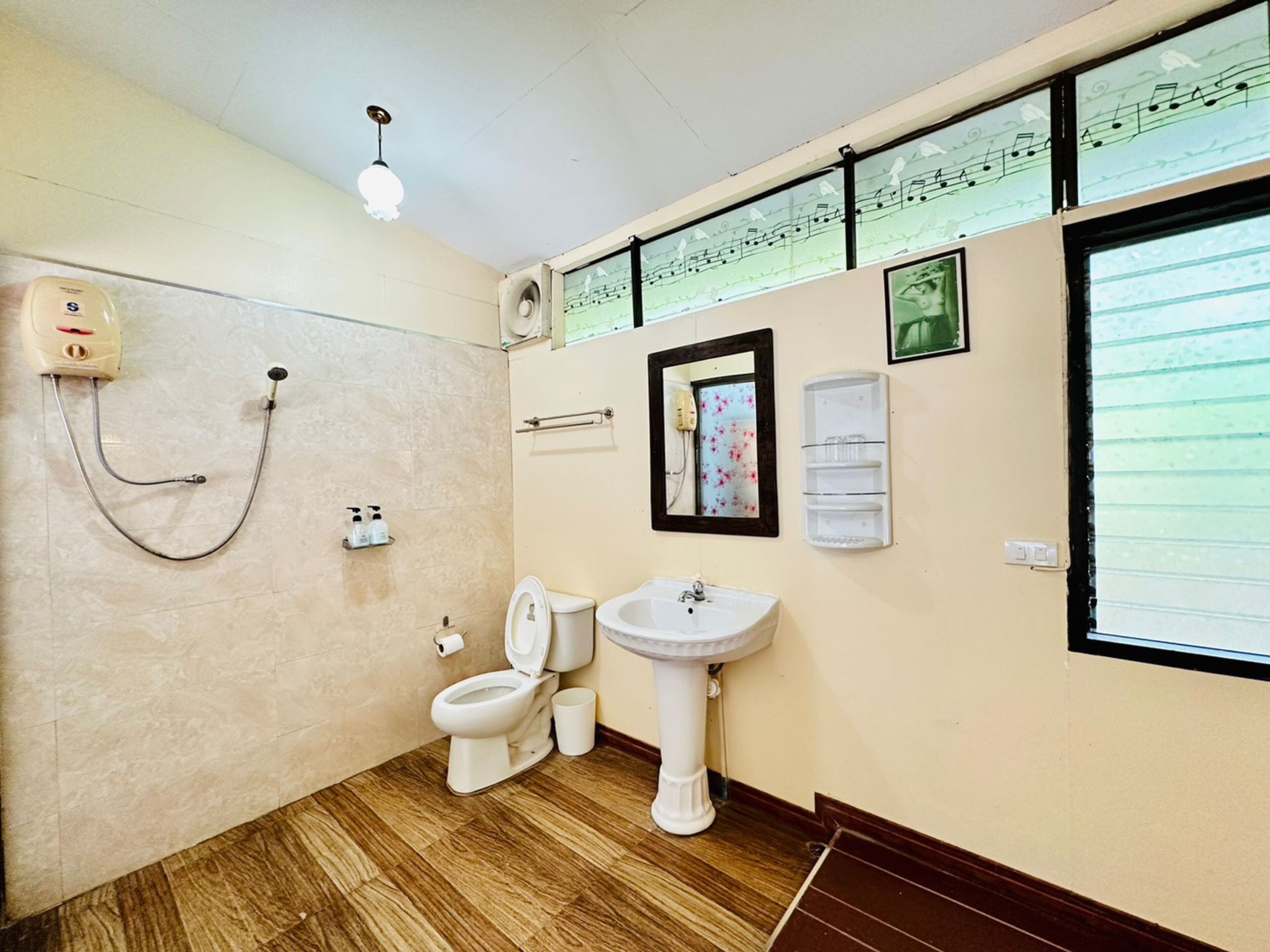 A bathroom with a toilet, sink, and shower. There are musical notes on the wall and a mirror.