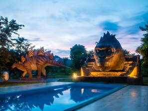 A dinosaur statue and a large rock formation with a pool in the foreground. - Yoko River Kwai Resort (Sai Yok)