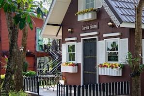 A building named "Carlos House" with a dark brown facade, white shutters, and flower boxes. - Yoko River Kwai Resort (Sai Yok)
