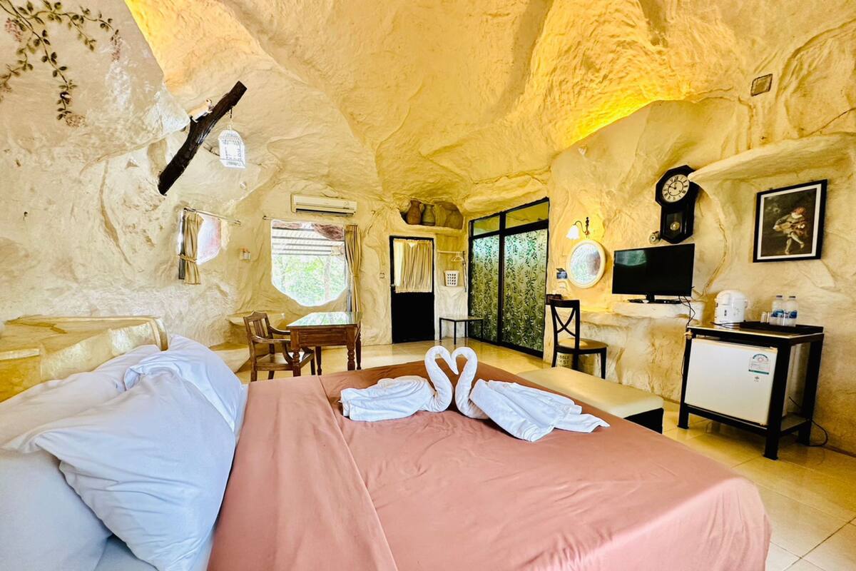 A cozy room with a bed, a desk, a chair, a TV, and a small fridge.