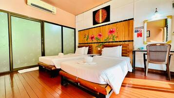 A hotel room with two beds, a wooden floor, a desk with a chair, and a large mirror.