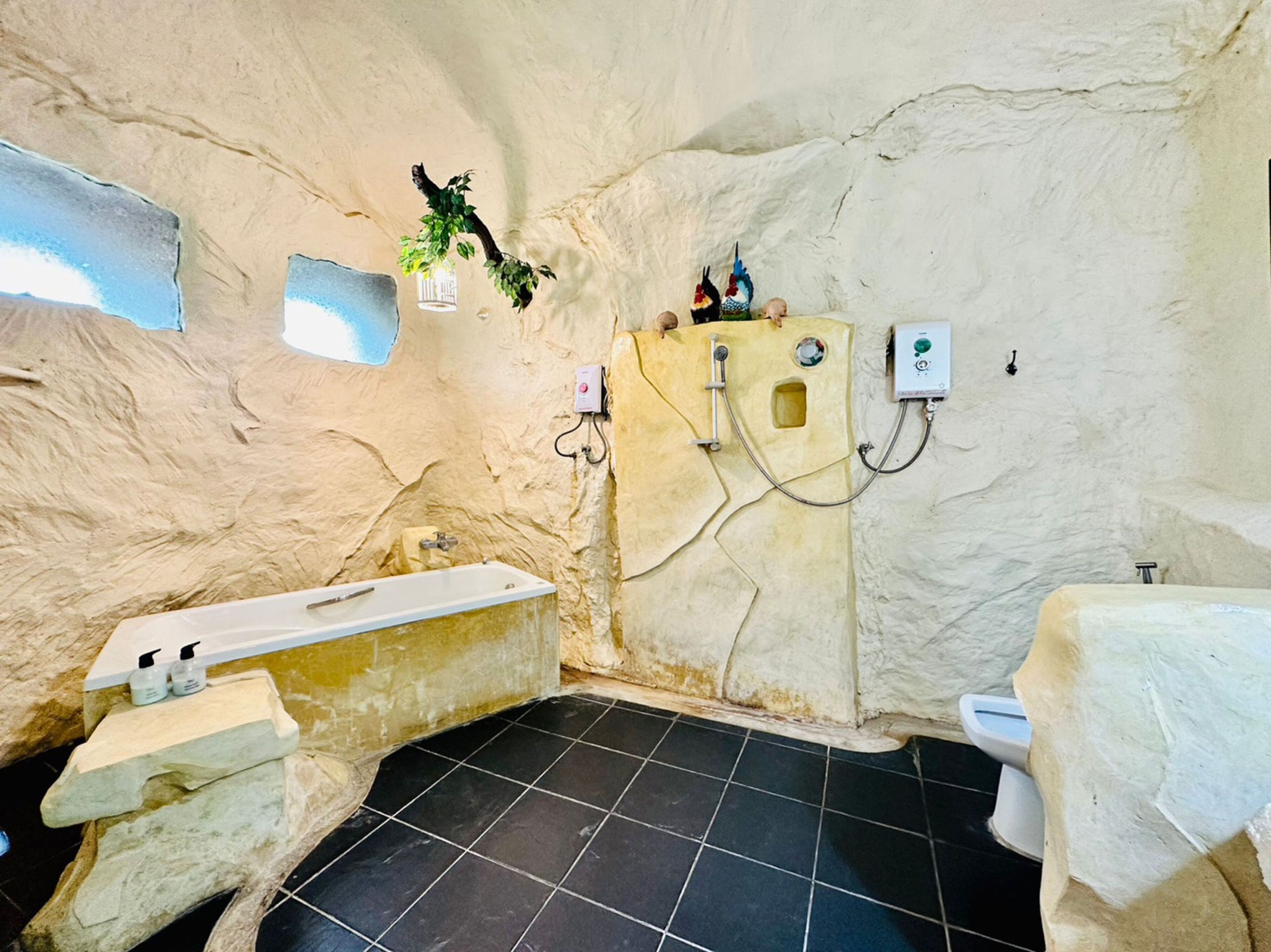 Un baño con bañera, inodoro y ducha. Hay dos enchufes en la pared.