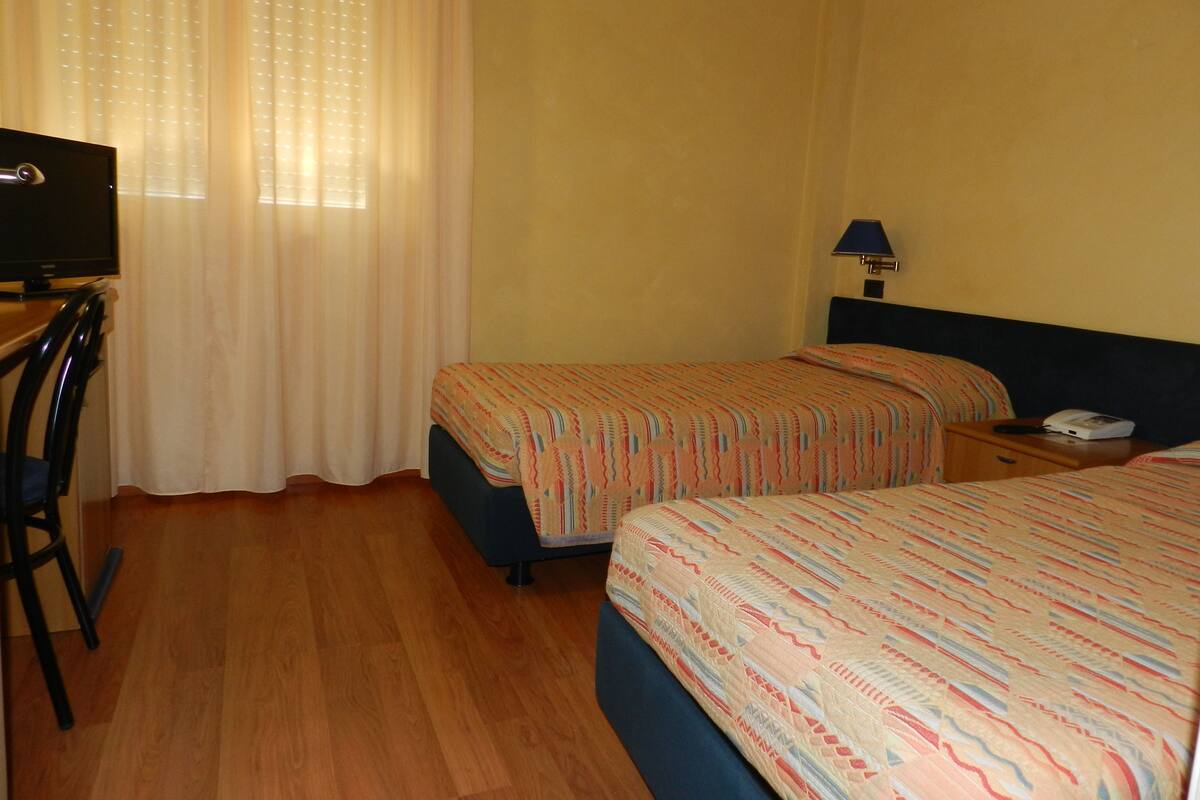 Ein Hotelzimmer mit zwei Betten, einem Schreibtisch, einem Stuhl, einer Lampe und einem Fernseher.
