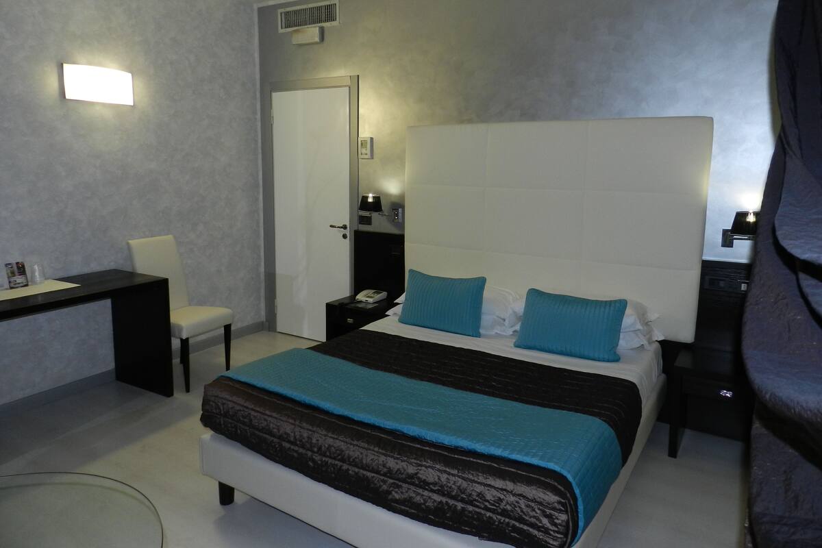Ein modernes Hotelzimmer mit einem großen Bett, einem Schreibtisch, einem Sessel und einem Nachttisch.